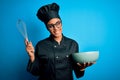 Young african american chef girl wearing cooker uniform and hat using whisk and bowl with a happy face standing and smiling with a Royalty Free Stock Photo