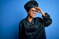 Young african american chef woman wearing cooker uniform and hat over blue background very happy and smiling looking far away with Royalty Free Stock Photo