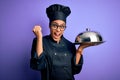 Young african american cooker girl wearing uniform and hat holding tray with dome screaming proud and celebrating victory and Royalty Free Stock Photo