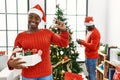 Young african american couple standing by christmas tree smiling and confident gesturing with hand doing small size sign with Royalty Free Stock Photo