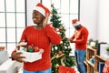 Young african american couple standing by christmas tree smiling with hand over ear listening an hearing to rumor or gossip