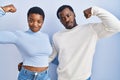 Young african american couple standing over blue background strong person showing arm muscle, confident and proud of power Royalty Free Stock Photo