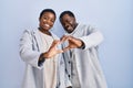 Young african american couple standing over blue background together smiling in love doing heart symbol shape with hands Royalty Free Stock Photo