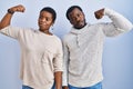 Young african american couple standing over blue background together strong person showing arm muscle, confident and proud of Royalty Free Stock Photo