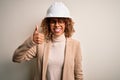 Young african american curly architect woman wearing safety helmet and glasses doing happy thumbs up gesture with hand Royalty Free Stock Photo