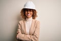 Young african american curly architect woman wearing safety helmet and glasses happy face smiling with crossed arms looking at the Royalty Free Stock Photo