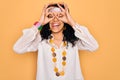 Young african american curly hippie woman wearing sunglasses and vintage accessories doing ok gesture like binoculars sticking