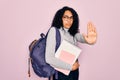 Young african american curly student woman wearing backpack and glasses holding book with open hand doing stop sign with serious Royalty Free Stock Photo