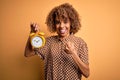 Young african american curly woman holding vintage alarm clock over yellow background screaming proud and celebrating victory and Royalty Free Stock Photo