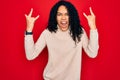 Young african american curly woman wearing casual turtleneck sweater over red background shouting with crazy expression doing rock Royalty Free Stock Photo