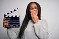 Young african american director girl filming a movie using clapboard over isolated background cover mouth with hand shocked with Royalty Free Stock Photo