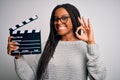 Young african american director girl filming a movie using clapboard over isolated background doing ok sign with fingers, Royalty Free Stock Photo