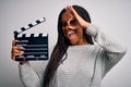 Young african american director girl filming a movie using clapboard over isolated background with happy face smiling doing ok Royalty Free Stock Photo