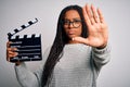 Young african american director girl filming a movie using clapboard over isolated background with open hand doing stop sign with Royalty Free Stock Photo