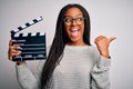 Young african american director girl filming a movie using clapboard over isolated background pointing and showing with thumb up