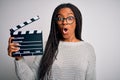 Young african american director girl filming a movie using clapboard over isolated background scared in shock with a surprise Royalty Free Stock Photo