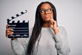 Young african american director girl filming a movie using clapboard over isolated background serious face thinking about Royalty Free Stock Photo