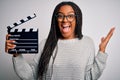 Young african american director girl filming a movie using clapboard over isolated background very happy and excited, winner Royalty Free Stock Photo