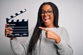 Young african american director girl filming a movie using clapboard over isolated background very happy pointing with hand and Royalty Free Stock Photo