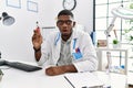 Young african american doctor man holding electronic cigarette at medical clinic scared and amazed with open mouth for surprise, Royalty Free Stock Photo