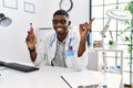 Young african american doctor man holding electronic cigarette at medical clinic smiling happy pointing with hand and finger to Royalty Free Stock Photo