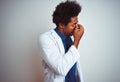 Young african american doctor man wearing coat standing over isolated white background tired rubbing nose and eyes feeling fatigue Royalty Free Stock Photo