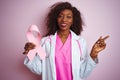 Young african american doctor woman holding cancer ribbon over isolated pink background very happy pointing with hand and finger