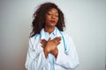 Young african american doctor woman wearing stethoscope over isolated white background smiling with hands on chest with closed Royalty Free Stock Photo