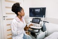 Young african-american female doctor in white coat using ultra ultrasound scanning machine and looking on the screen Royalty Free Stock Photo