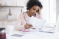 African woman feeling stressed while managing family budget at kitchen table Royalty Free Stock Photo