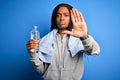 Young african american fitness woman wearing towel and drinking water from plastic bottle with open hand doing stop sign with Royalty Free Stock Photo