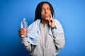 Young african american fitness woman wearing towel and drinking water from plastic bottle serious face thinking about question, Royalty Free Stock Photo