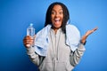 Young african american fitness woman wearing towel and drinking water from plastic bottle very happy and excited, winner