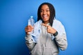 Young african american fitness woman wearing towel and drinking water from plastic bottle very happy pointing with hand and finger