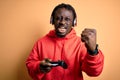 Young african american gamer man playing video game using joystick and headphones annoyed and frustrated shouting with anger, Royalty Free Stock Photo