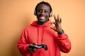 Young african american gamer man playing video game using joystick and headphones doing ok sign with fingers, excellent symbol Royalty Free Stock Photo