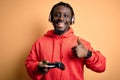 Young african american gamer man playing video game using joystick and headphones happy with big smile doing ok sign, thumb up Royalty Free Stock Photo