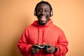 Young african american gamer man playing video game using joystick and headphones with a happy face standing and smiling with a Royalty Free Stock Photo