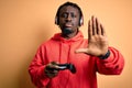 Young african american gamer man playing video game using joystick and headphones with open hand doing stop sign with serious and Royalty Free Stock Photo