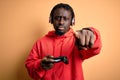 Young african american gamer man playing video game using joystick and headphones pointing with finger to the camera and to you, Royalty Free Stock Photo
