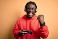 Young african american gamer man playing video game using joystick and headphones screaming proud and celebrating victory and Royalty Free Stock Photo