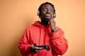 Young african american gamer man playing video game using joystick and headphones serious face thinking about question, very Royalty Free Stock Photo