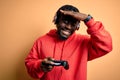 Young african american gamer man playing video game using joystick and headphones stressed with hand on head, shocked with shame Royalty Free Stock Photo