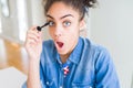 Young african american girl applying eyelashes mascara scared in shock with a surprise face, afraid and excited with fear Royalty Free Stock Photo