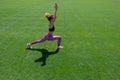 A young African-American girl in a black T-shirt, pink pants and sneakers doing sports exercises on green grass and Royalty Free Stock Photo