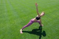 A young African-American girl in a black T-shirt, pink pants and sneakers doing sports exercises on green grass and raising her ha Royalty Free Stock Photo