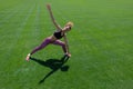A young African-American girl in a black T-shirt, pink pants and sneakers doing sports exercises on green grass and raising her ha Royalty Free Stock Photo