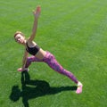 Modern style of life. A young African-American girl in a black T-shirt, pink pants and sneakers doing sports exercises on green gr Royalty Free Stock Photo