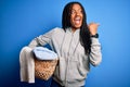 Young african american girl doing domestic housework holding laundry wicker basket pointing and showing with thumb up to the side