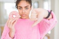 Young african american girl eating sweet pink donut with angry face, negative sign showing dislike with thumbs down, rejection